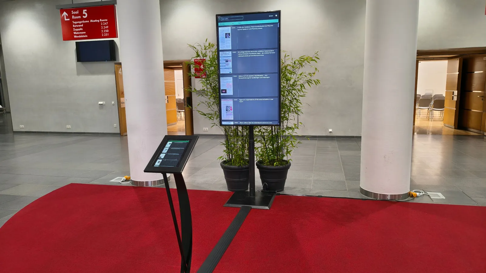 ePoster-Station im Kongressfoyer mit Posterübersicht auf dem Bildschirm und Tablet-Pult zur Steuerung